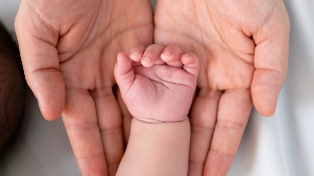 Adoption. Image of a pair of adult's hands holding a baby's hands in their open palm.