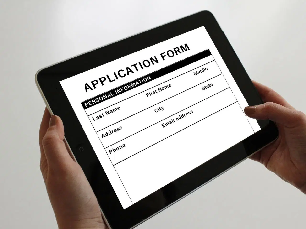 Person holding a tablet displaying an application form. The form includes sections for personal information: Last Name, First Name, Middle, City, State, Address, Phone, and Email Address.