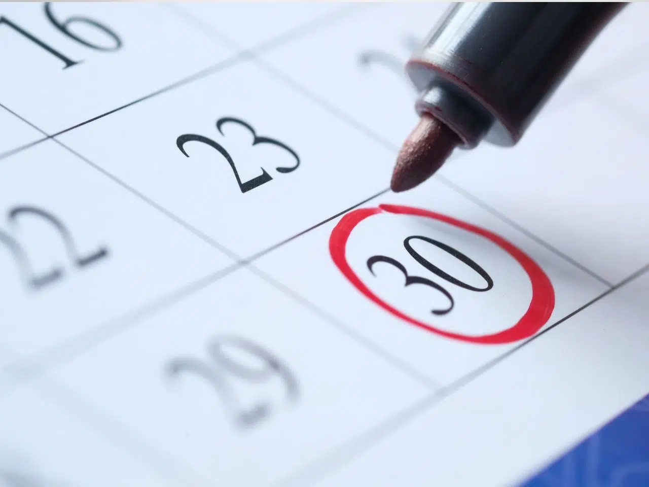 A close-up image of a calendar page showing the numbers 23, 29, and 30. The number 30 is circled in red, and a pen with a red tip hovers above the circle, emphasizing the date.