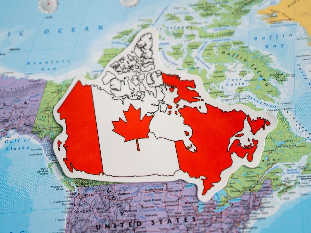 A map of Canada is overlaid with the Canadian flag, featuring a red maple leaf. The background shows parts of North America and surrounding oceans, including the Atlantic.