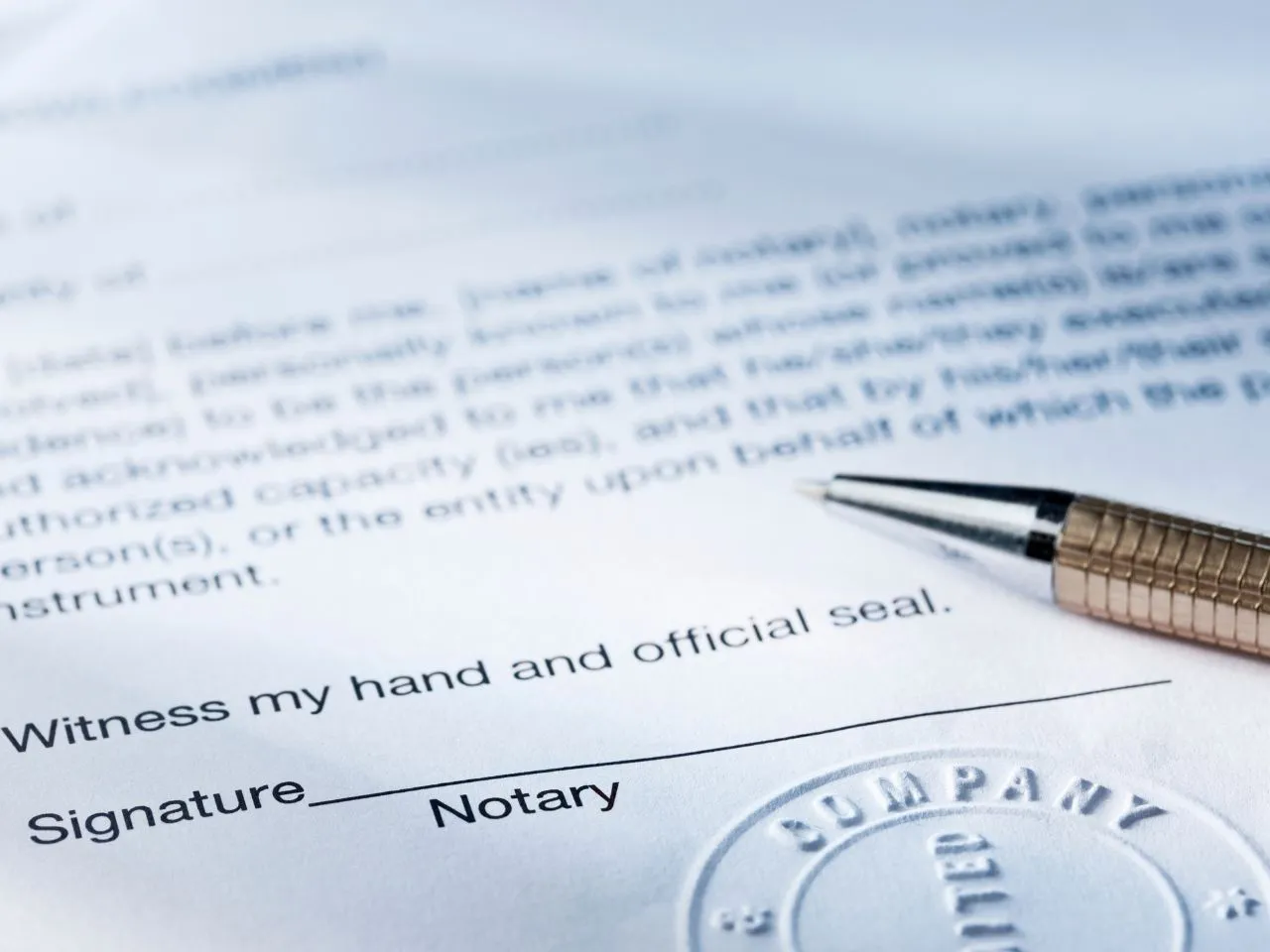 Close-up of a document with text and a signature line labeled Signature and Notary. There is a pen placed diagonally across the paper, and part of a circular notary seal is visible at the bottom right corner.