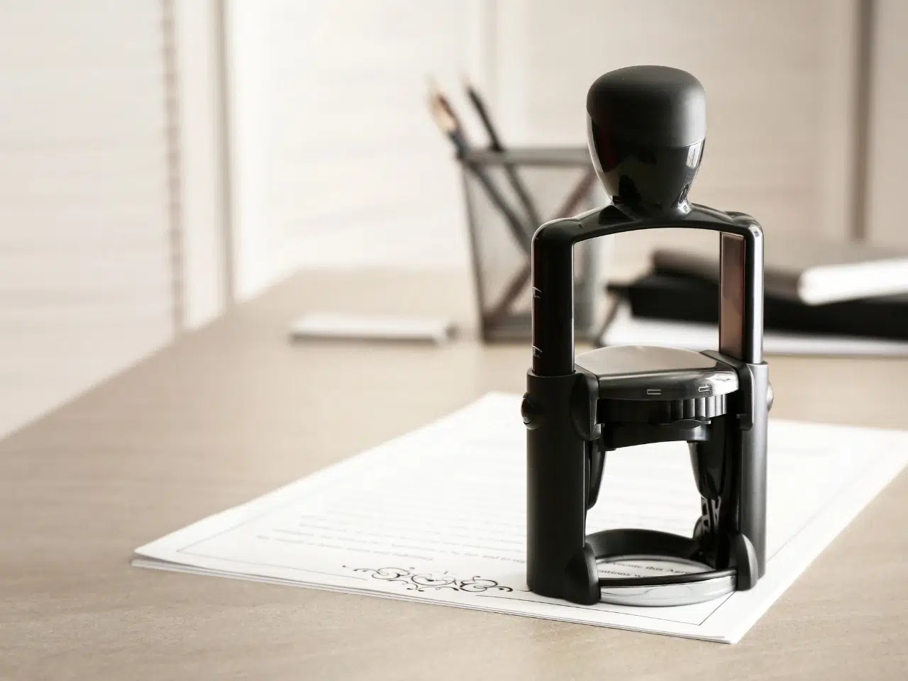 A black notary stamp sits on top of a document on a desk, with blurred office supplies and paperwork in the background.