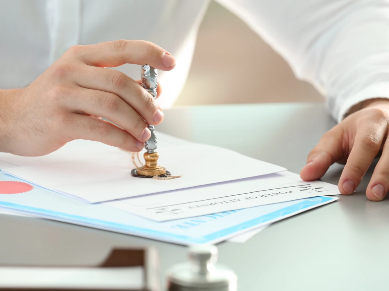 A person presses a wax seal stamp onto a document on a desk, signifying UAE embassy Canada authentication or approval of official paperwork. Other documents and a blurred ink bottle are visible nearby.