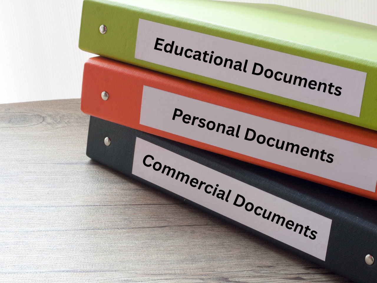 Three binders stacked on a wooden surface, labeled Educational Documents (green binder), Personal Documents (orange binder), and Commercial Documents (black binder).