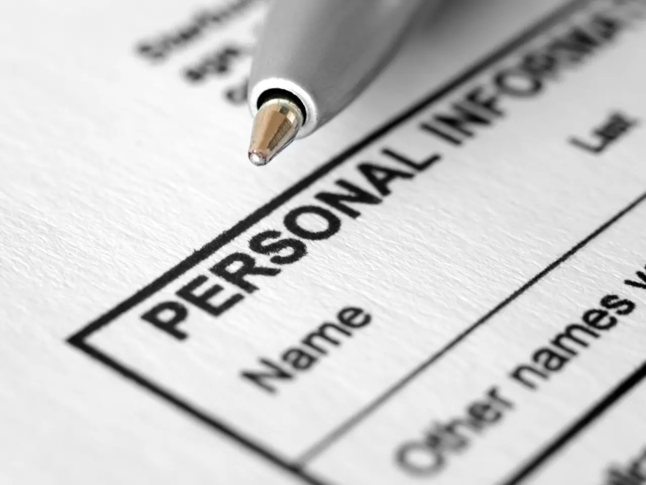 A close-up of a pen resting on a form labeled PERSONAL INFO, with lines underneath for entering a name and other details. The focus is on the text and the pen tip.