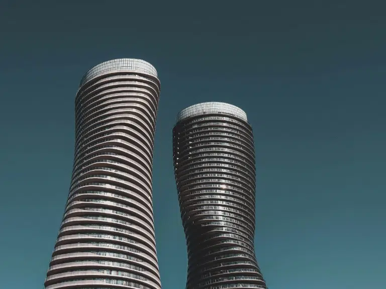Two modern, curving high-rise buildings with a twisted design stand against a clear blue sky, their glass and white exterior creating an elegant, futuristic appearance.