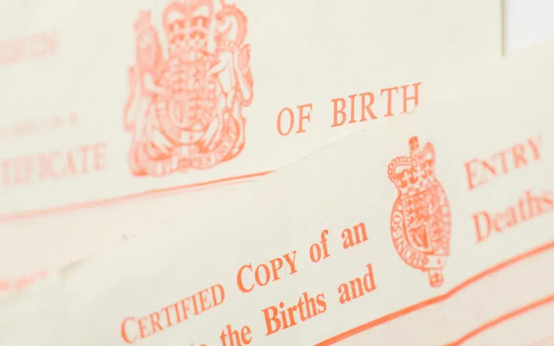 Close-up of UK birth and death certificates, showing official red crests, partial text CERTIFIED COPY of an ENTRY, BIRTHS and, and parts of the words BIRTH and DEATHS.