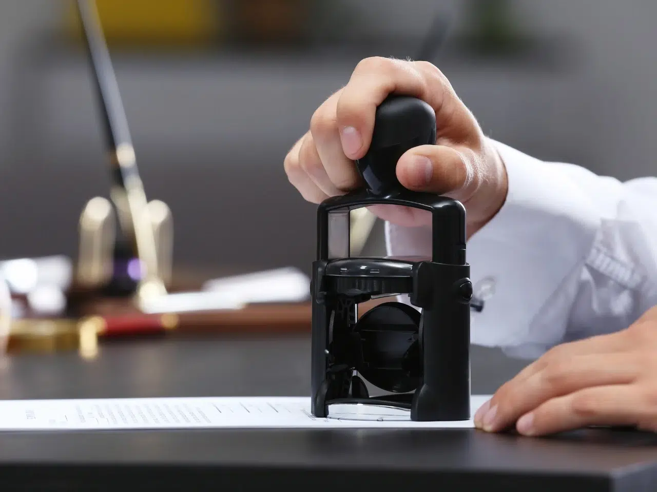 A person presses a black stamp onto a document on a desk, suggesting the process of official approval or authentication.