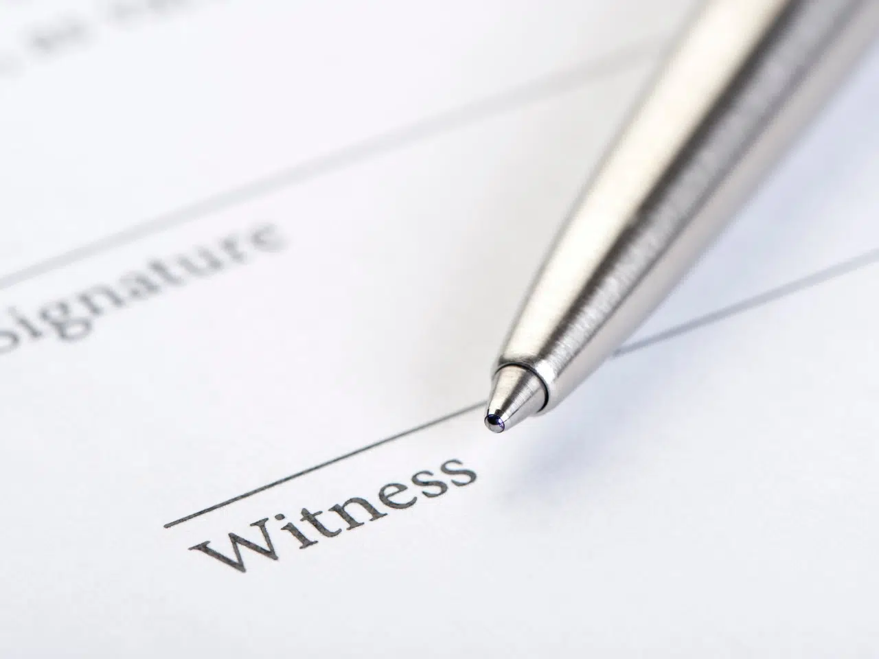A close-up of a pen poised above a document, focusing on the word Witness next to a signature line, suggesting the document is ready to be signed by a witness.