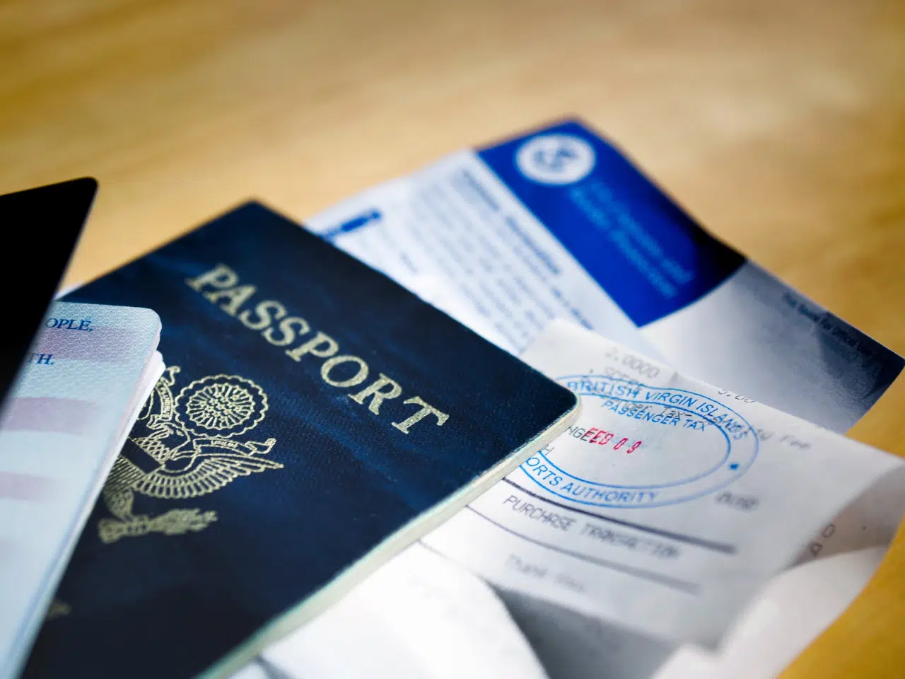 A close-up of a blue United States passport, immigration documents, and a travel visa stamp, all spread out on a wooden surface.