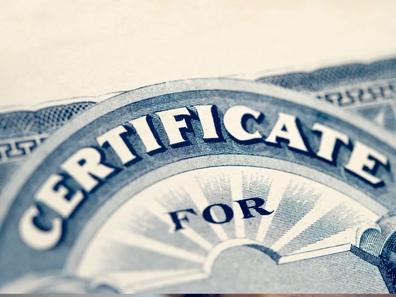 Close-up of a certificate with the partial word “CERTIFICATE” and “FOR” visible, featuring ornate blue detailing and a decorative sunburst pattern in the background.
