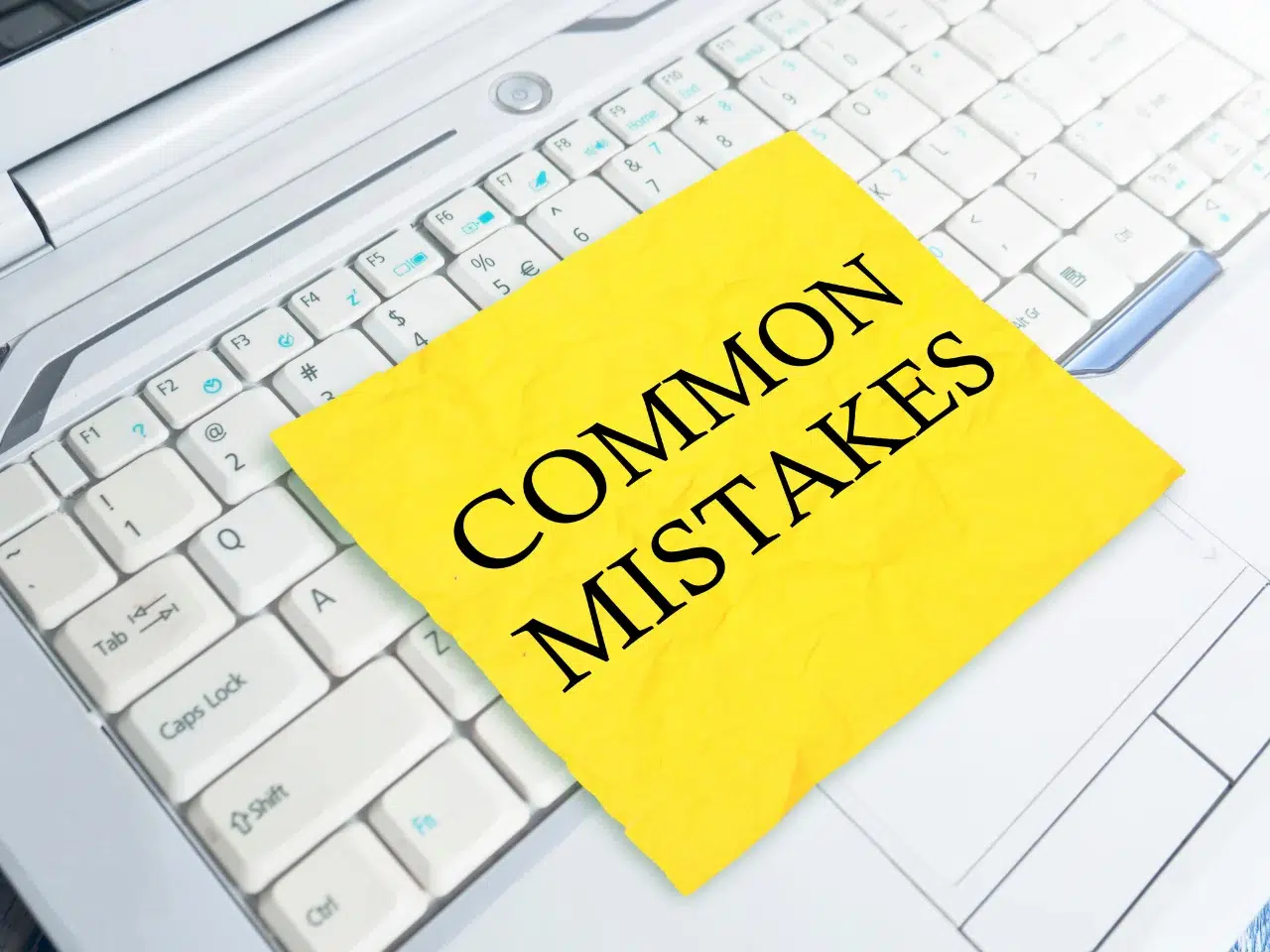 A yellow sticky note with the words COMMON MISTAKES in bold black letters is placed on the white keyboard of a laptop.