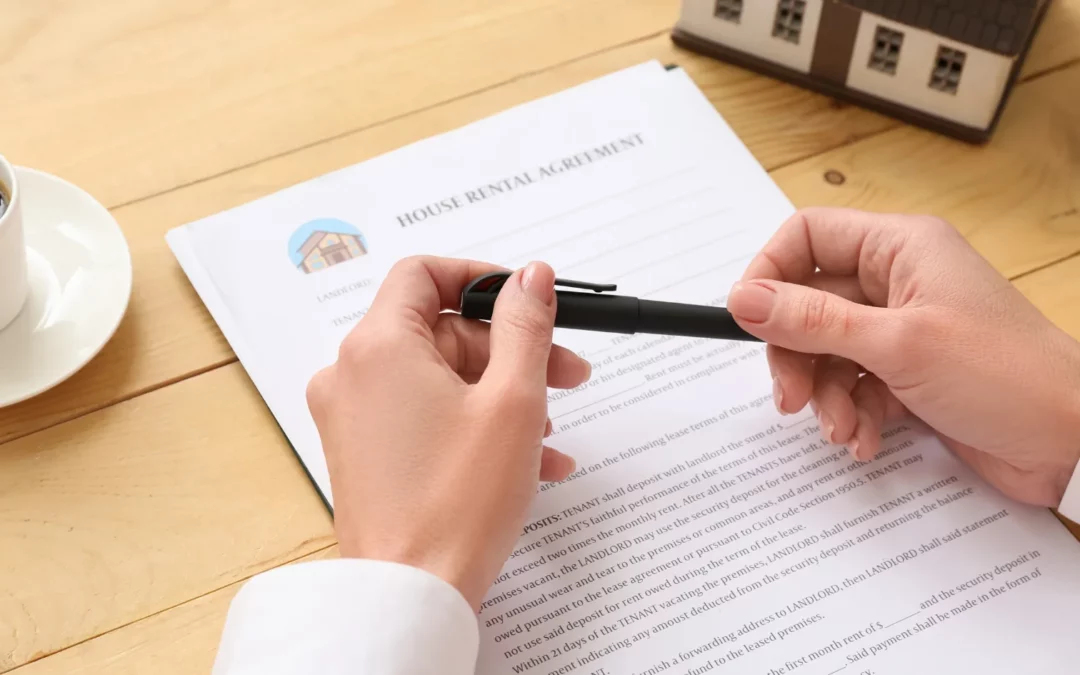 A person holding a pen sits at a wooden table with a cup of coffee, a model house, and a house rental agreement document ready to be signed.