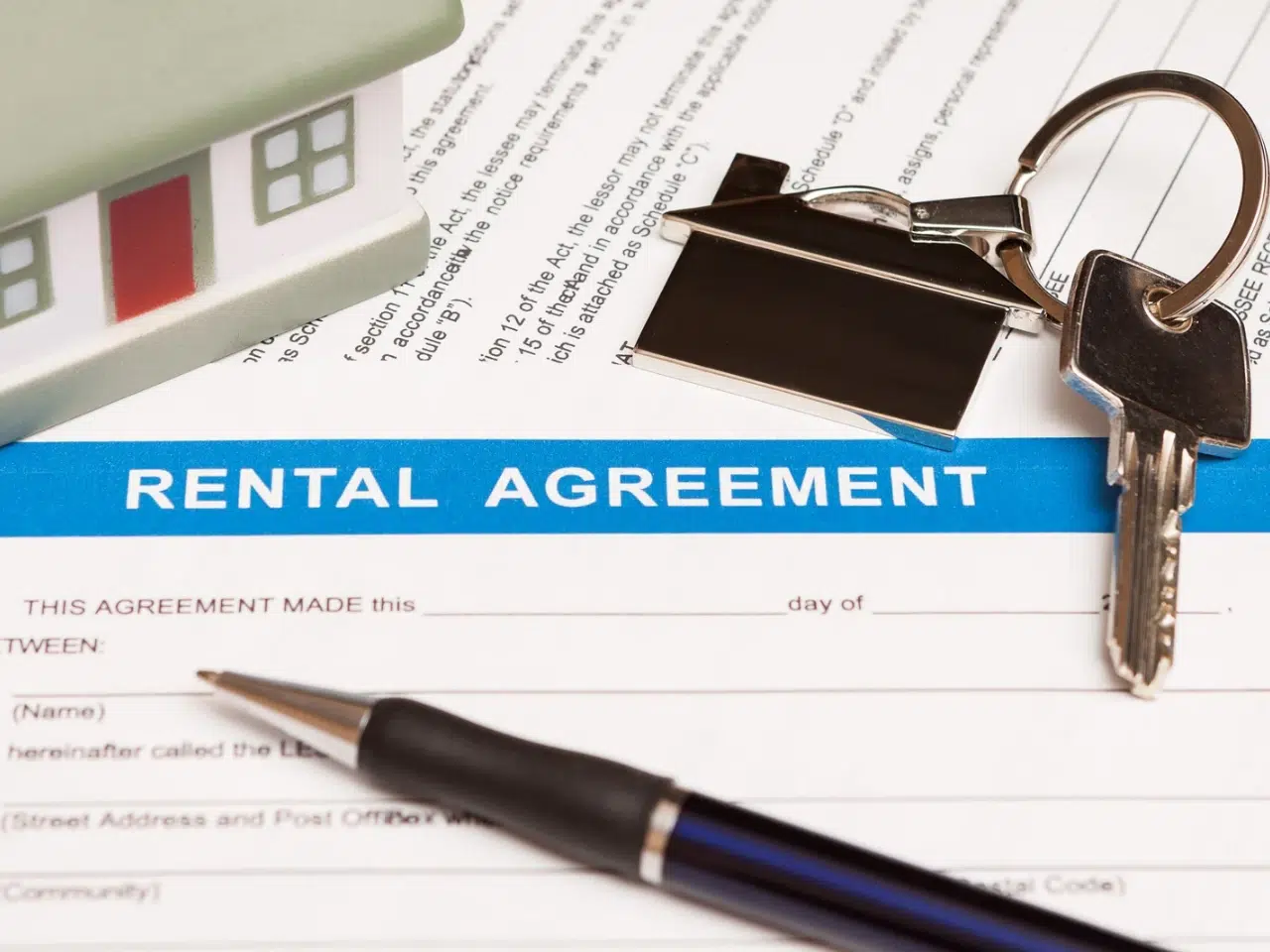 A rental agreement form with a blue header is shown alongside a pen, a pair of house keys with a house-shaped keychain, and a small model house.