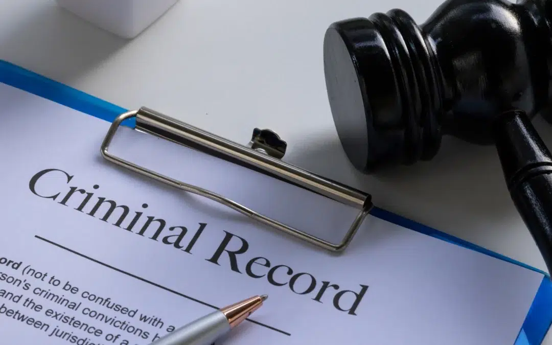 A clipboard holding a document labeled Criminal Record next to a pen and a judges gavel on a white desk.