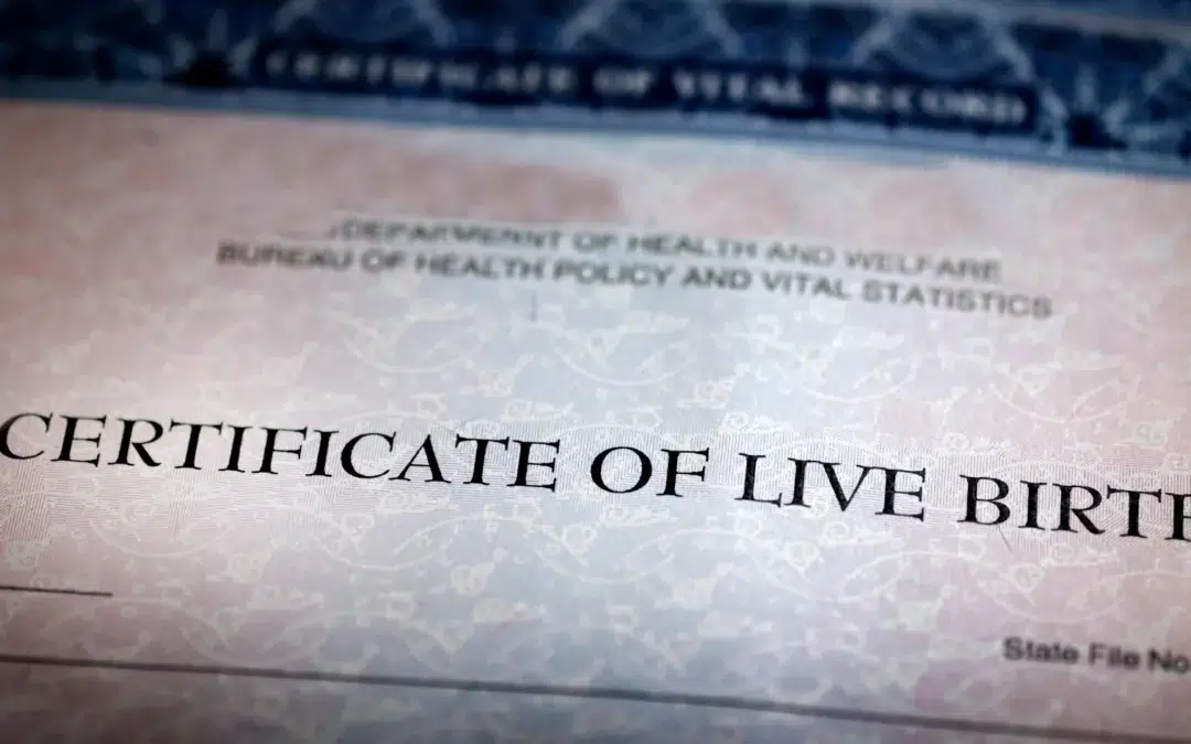 A close-up of a certificate of live birth, showing the heading in large, bold letters. The background features a decorative security pattern and partial text from a government health department.
