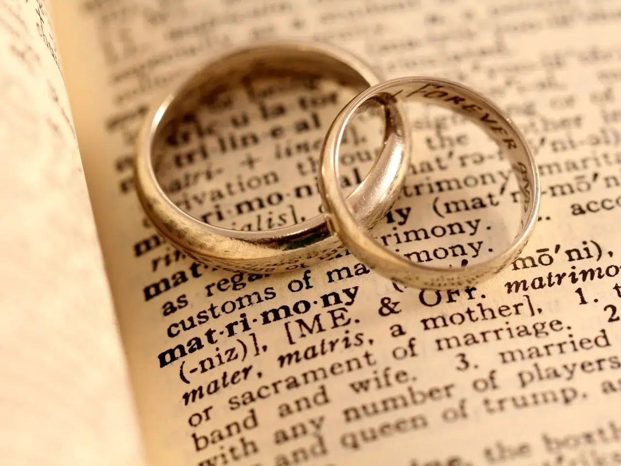 Two gold wedding rings rest on an open dictionary, highlighting the word matrimony and its definition.