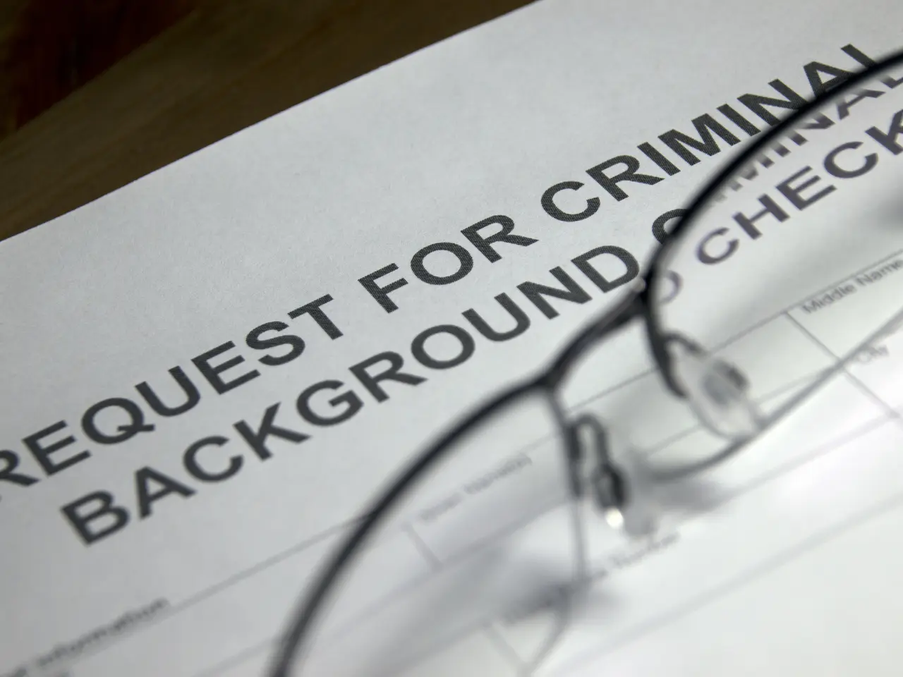 A close-up of a document titled Request for Criminal Background Check with a pair of eyeglasses resting on top of the paper.