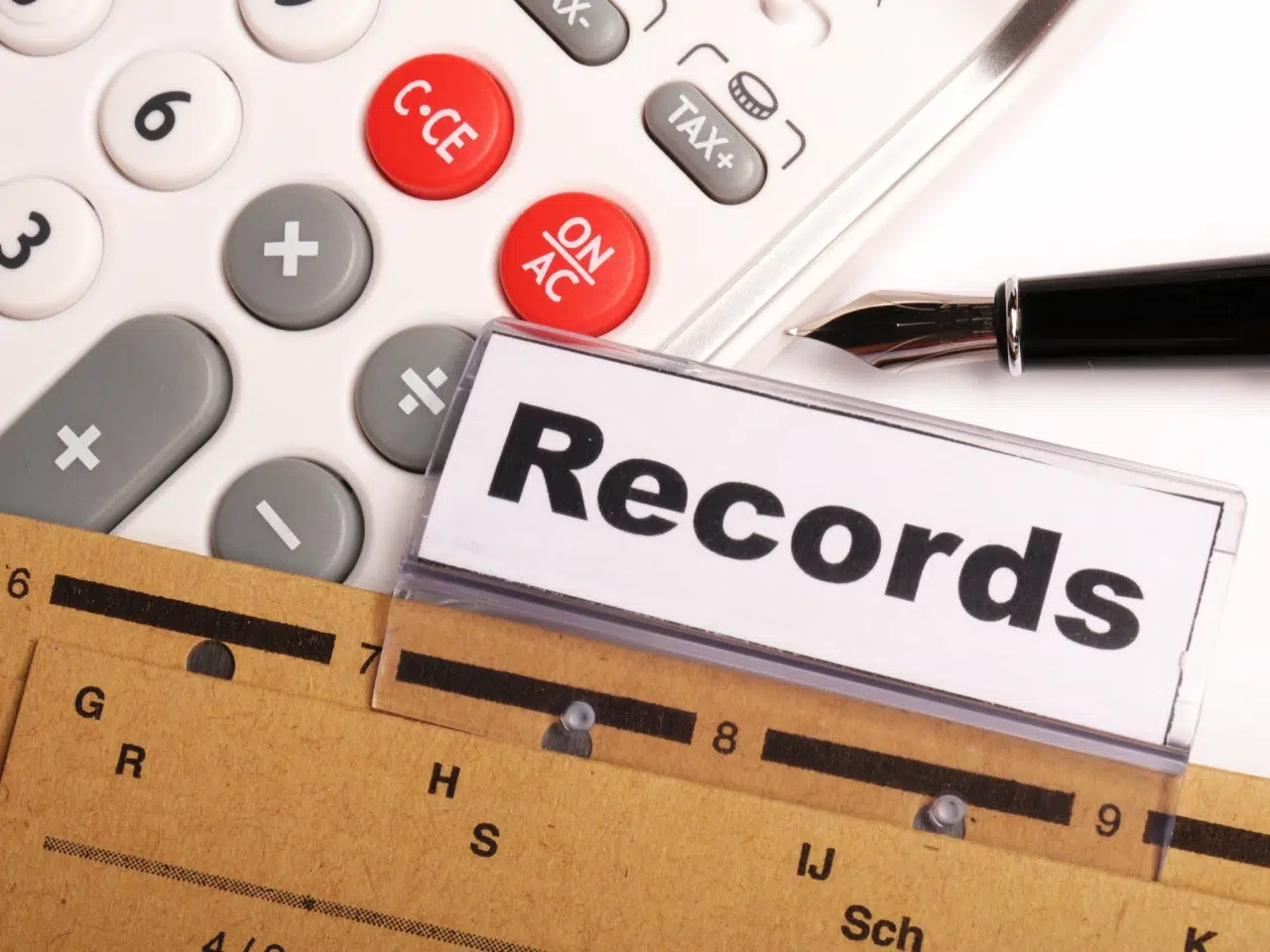 A close-up of a calculator, a pen, a folder labeled Records, and a ruler, representing bookkeeping or financial record-keeping.