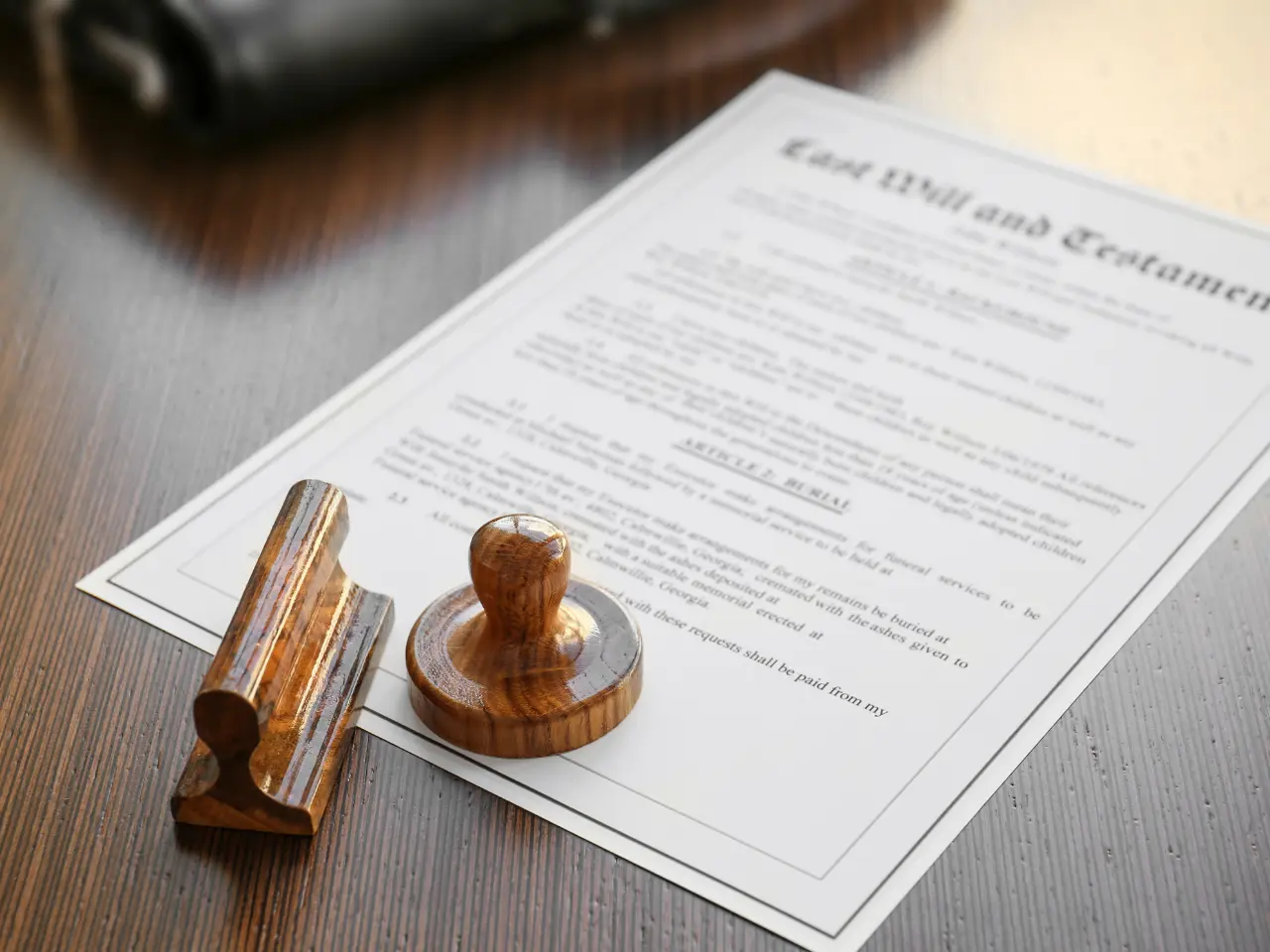 A legal document titled Last Will and Testament lies on a wooden surface beside a wooden stamp and holder. The document appears ready for signing or approval.