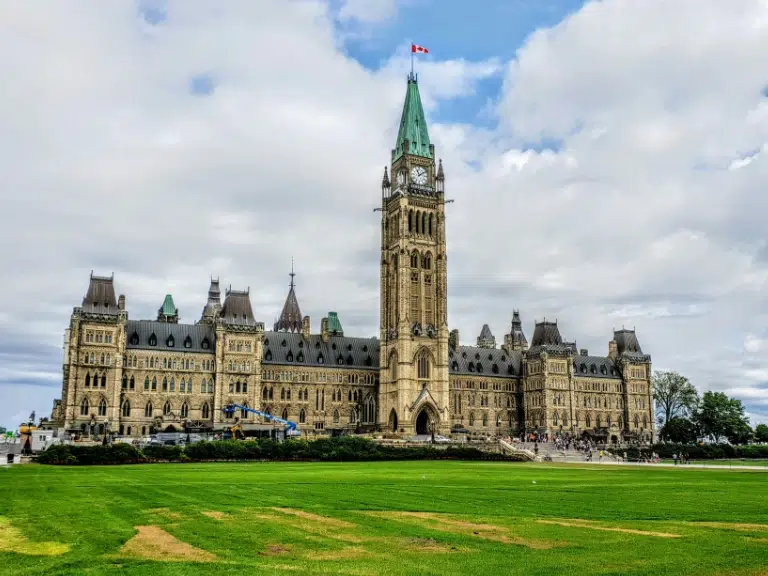 A close-up of a fingertip covered in black ink, showing detailed fingerprint ridges. In the background, a fingerprint impression is visible on a white surface, commonly used by RCMP accredited fingerprinting companies.
