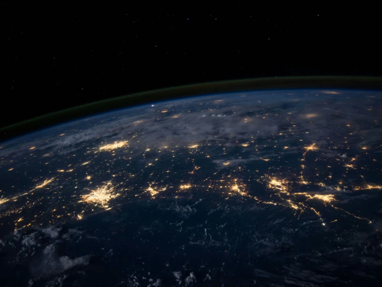 View of Earth from space at night, showing illuminated cities and towns connected by glowing lines—like networks linking rcmp accredited fingerprinting companies—beneath a thin atmospheric layer along the planet's curve against the dark backdrop of space.