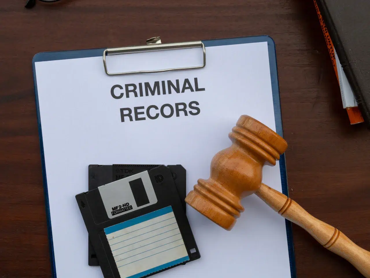 A clipboard with a paper titled CRIMINAL RECORS (misspelled), two floppy disks, and a wooden judges gavel resting on a dark wooden surface.