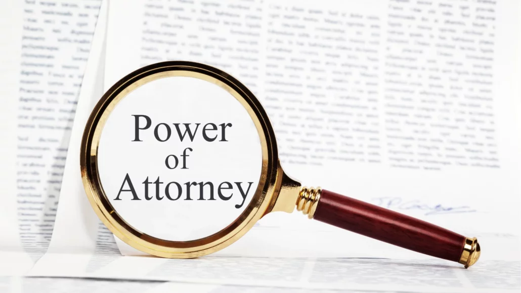 A magnifying glass with a wooden handle focuses on the words Power of Attorney printed on a document, with blurred legal text visible in the background.
