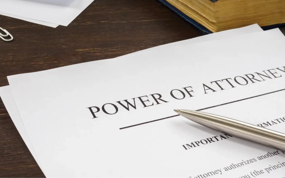 A close-up of a document titled Power of Attorney on a desk. A silver pen rests on the paper, and a thick book and paperclip are visible nearby.