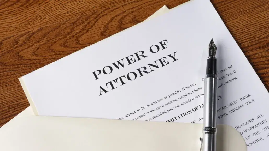 A Power of Attorney document partially pulled out of a cream-colored folder rests on a wooden desk next to a black and silver fountain pen.