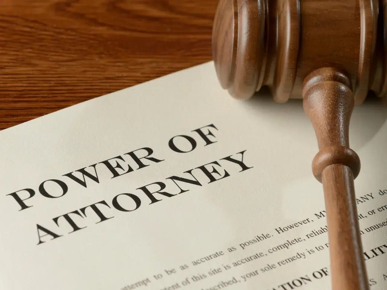 A close-up of a document titled POWER OF ATTORNEY lying on a wooden desk, with part of a wooden judge’s gavel resting on the page.