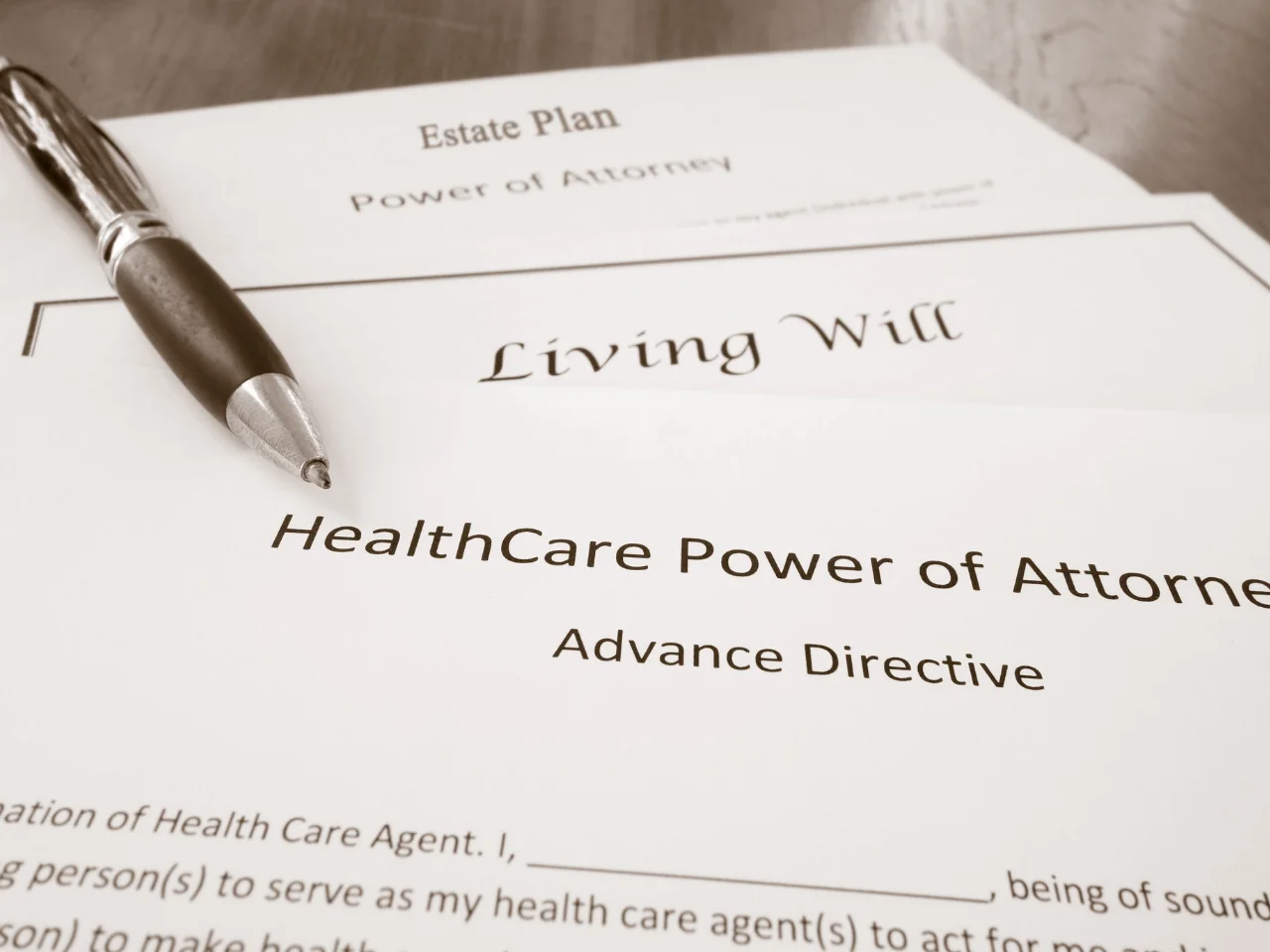 A close-up of legal documents labeled Estate Plan, Living Will, and Healthcare Power of Attorney with a pen resting on top. The papers relate to advance directives and power of attorney.