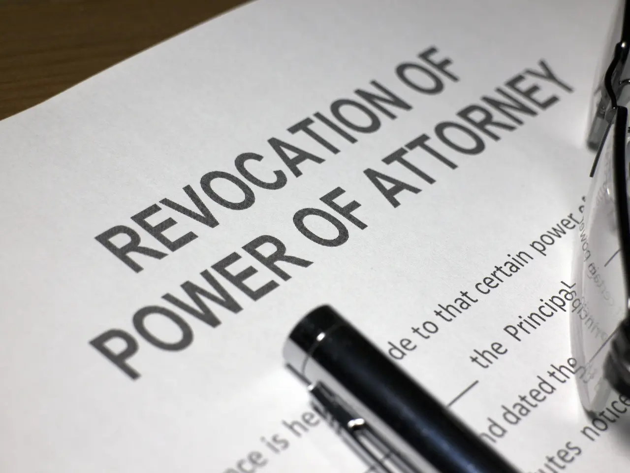 A close-up photo of a document titled Revocation of Power of Attorney with part of a black pen resting on the paper.