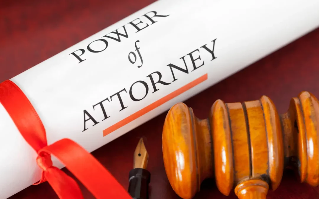A scroll labeled Power of Attorney tied with a red ribbon lies next to a wooden judges gavel and a fountain pen on a reddish surface.