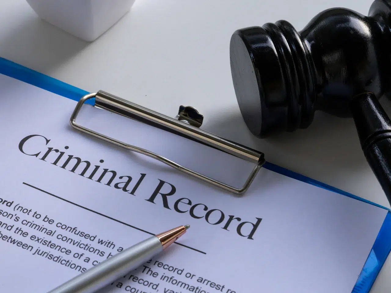 A document labeled Criminal Record on a clipboard, with a pen resting on it and a judges gavel placed nearby on the table.