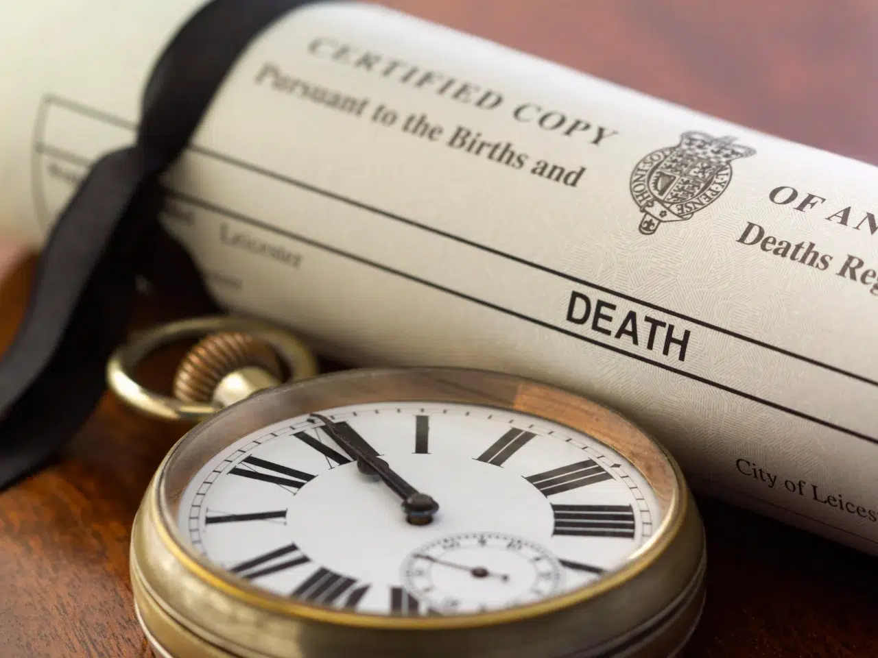 A close-up of a rolled death certificate with a black ribbon next to an antique pocket watch, symbolizing the passage of time and loss.