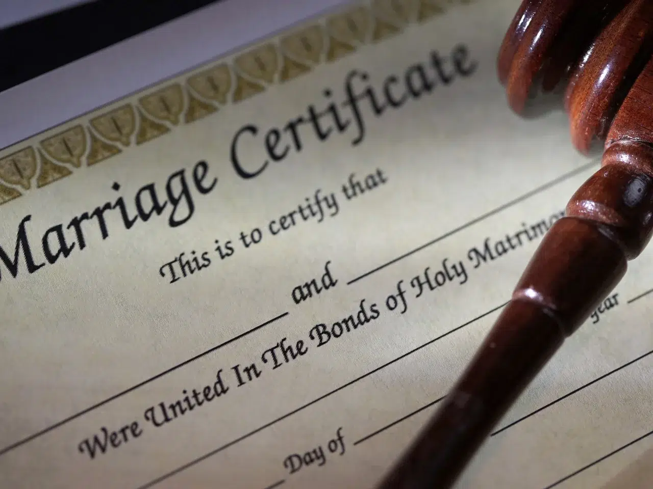 A close-up of a marriage certificate form with blank spaces for names and dates, partially covered by a wooden judges gavel, symbolizing legal recognition of marriage.