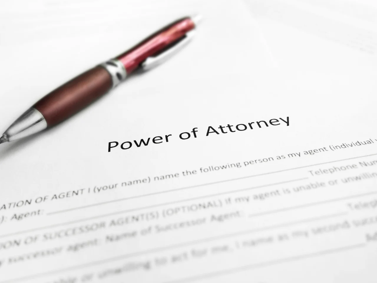 A close-up of a Power of Attorney document with a red and silver pen resting on top. The form includes spaces for agent details and appears ready to be filled out.
