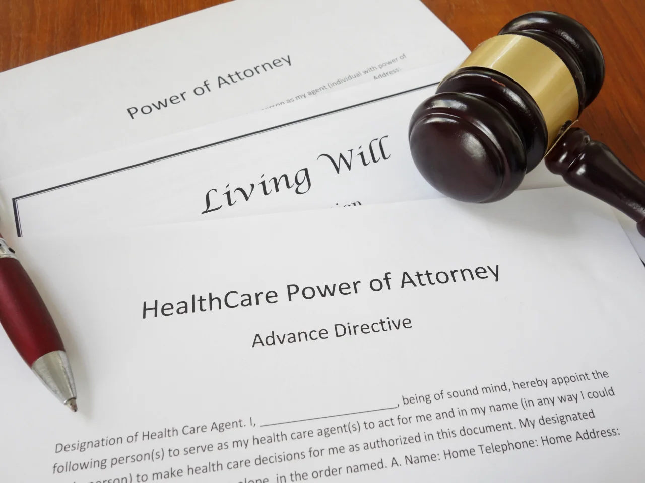 A close-up of legal documents labeled Power of Attorney, Living Will, and Healthcare Power of Attorney Advance Directive, with a wooden gavel resting beside them.