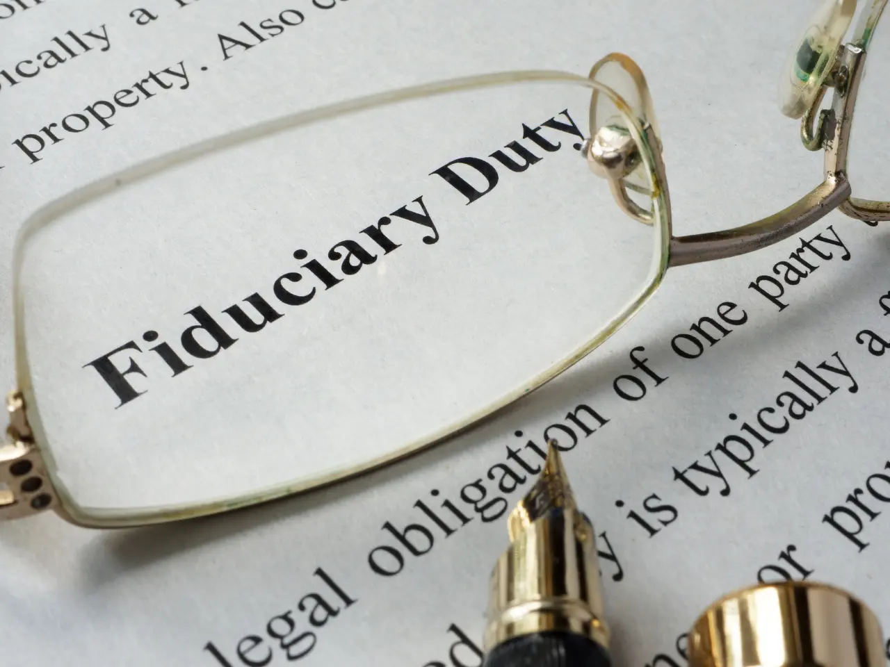 A pair of eyeglasses and a fountain pen rest on a document with the bold words “Fiduciary Duty” visible through the glasses, emphasizing the importance of the term.