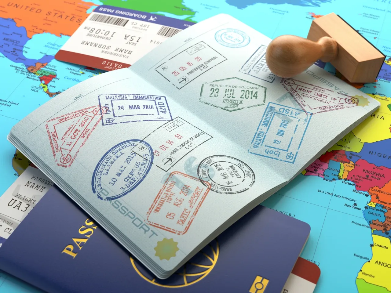 A passport open to pages covered in colorful visa stamps rests on a world map. Nearby are a wooden stamp, more passport covers, and airline boarding passes, symbolizing international travel.