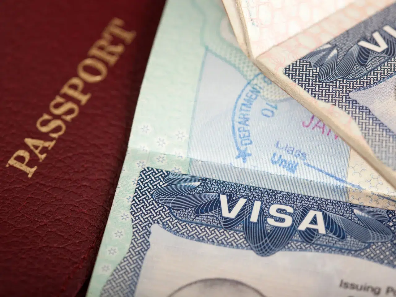 Close-up of a maroon passport next to two visa documents, with the word VISA clearly visible on the papers. The images suggest themes of travel, immigration, or international identification.