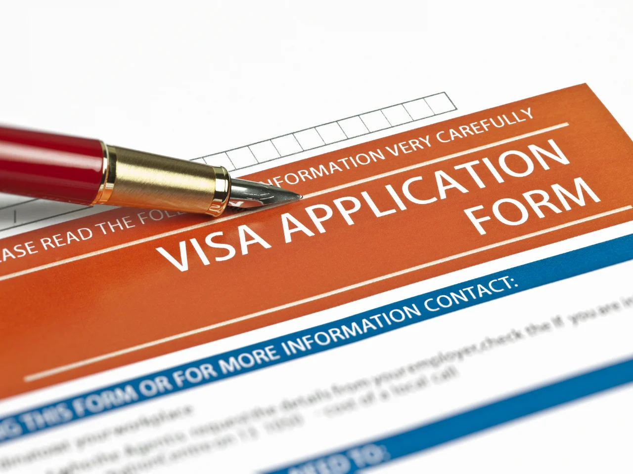A close-up of a visa application form with a red and gold pen resting on it. The words Visa Application Form are clearly visible in bold white letters on an orange background.