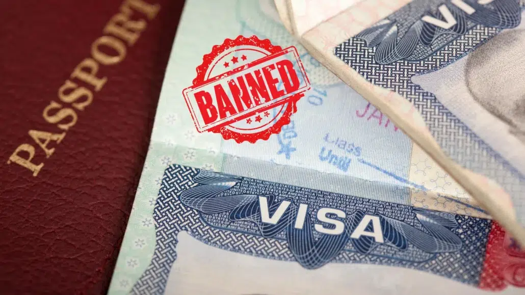 A close-up of a passport and a visa document, with a red BANNED stamp prominently displayed over the visa, indicating entry denial or travel restrictions.
