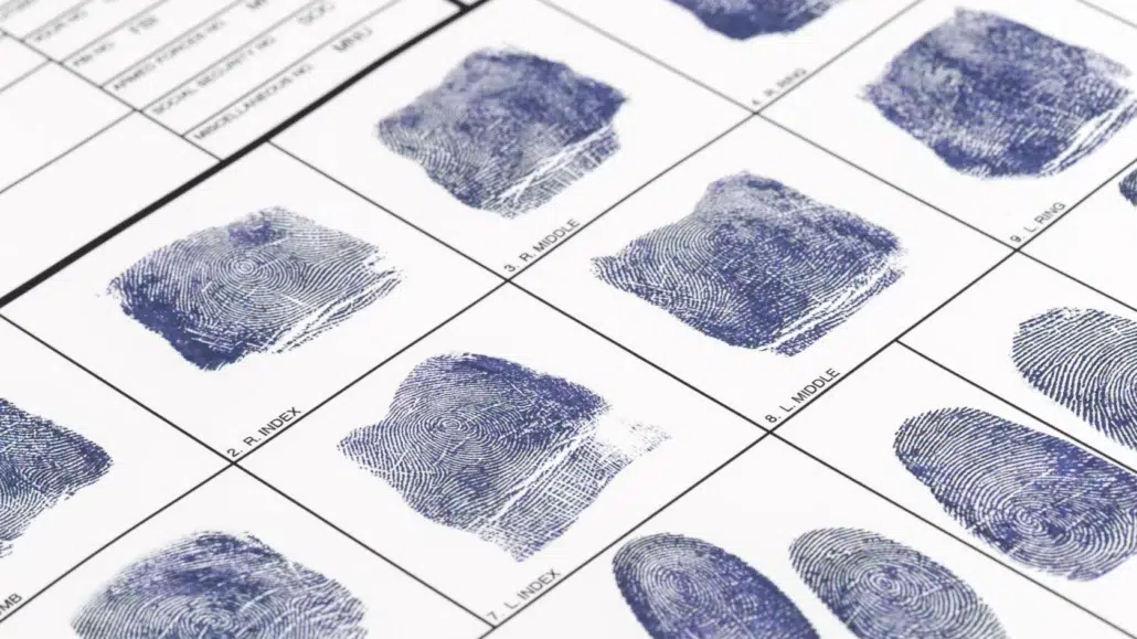 A close-up of a fingerprint identification card showing multiple inked fingerprints and labeled sections for different fingers, including areas marked R. INDEX and L. INDEX.