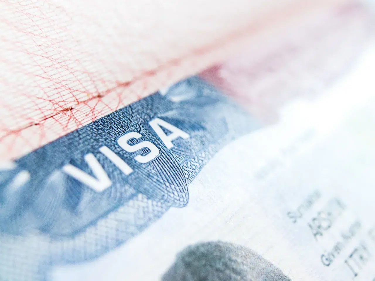 Close-up of a U.S. visa document, with the word VISA clearly visible in bold white letters on a blue background, showing intricate security patterns and part of the document’s textured surface.
