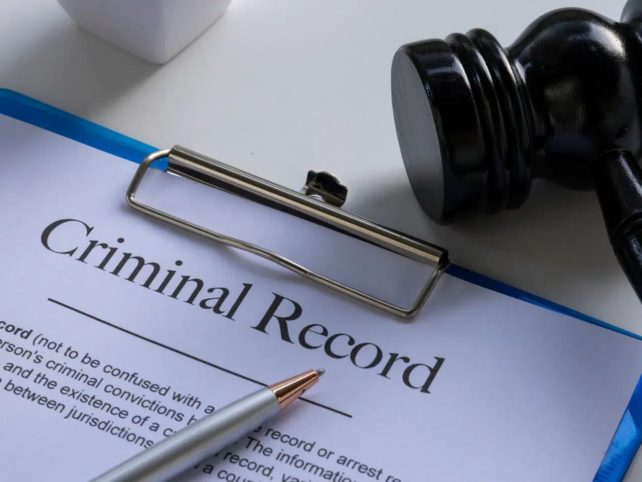 A clipboard holding a document labeled Criminal Record, with a pen resting on the paper and a judges gavel nearby on the desk.