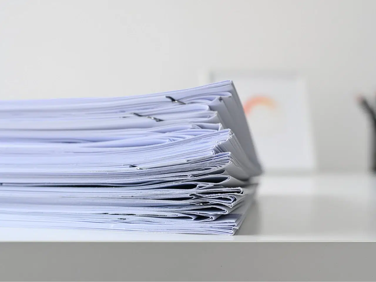A close-up of several stacks of paper documents clipped together, placed on a white desk with a blurred background.