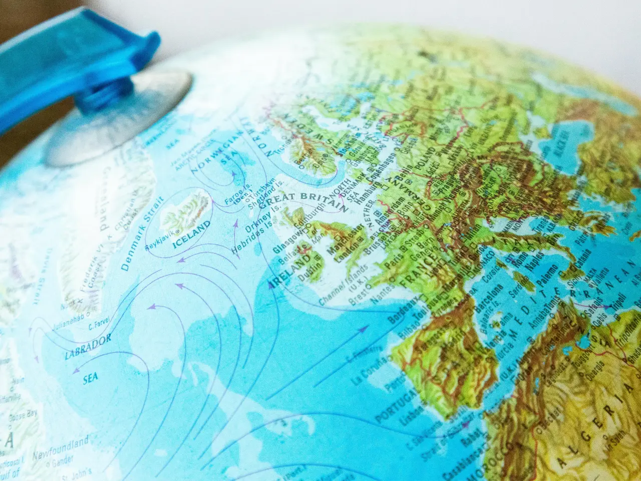 Close-up of a globe showing parts of Europe, including the United Kingdom, France, Spain, Germany, and the surrounding Atlantic Ocean with currents marked by arrows. The colors highlight land elevations and water depths.