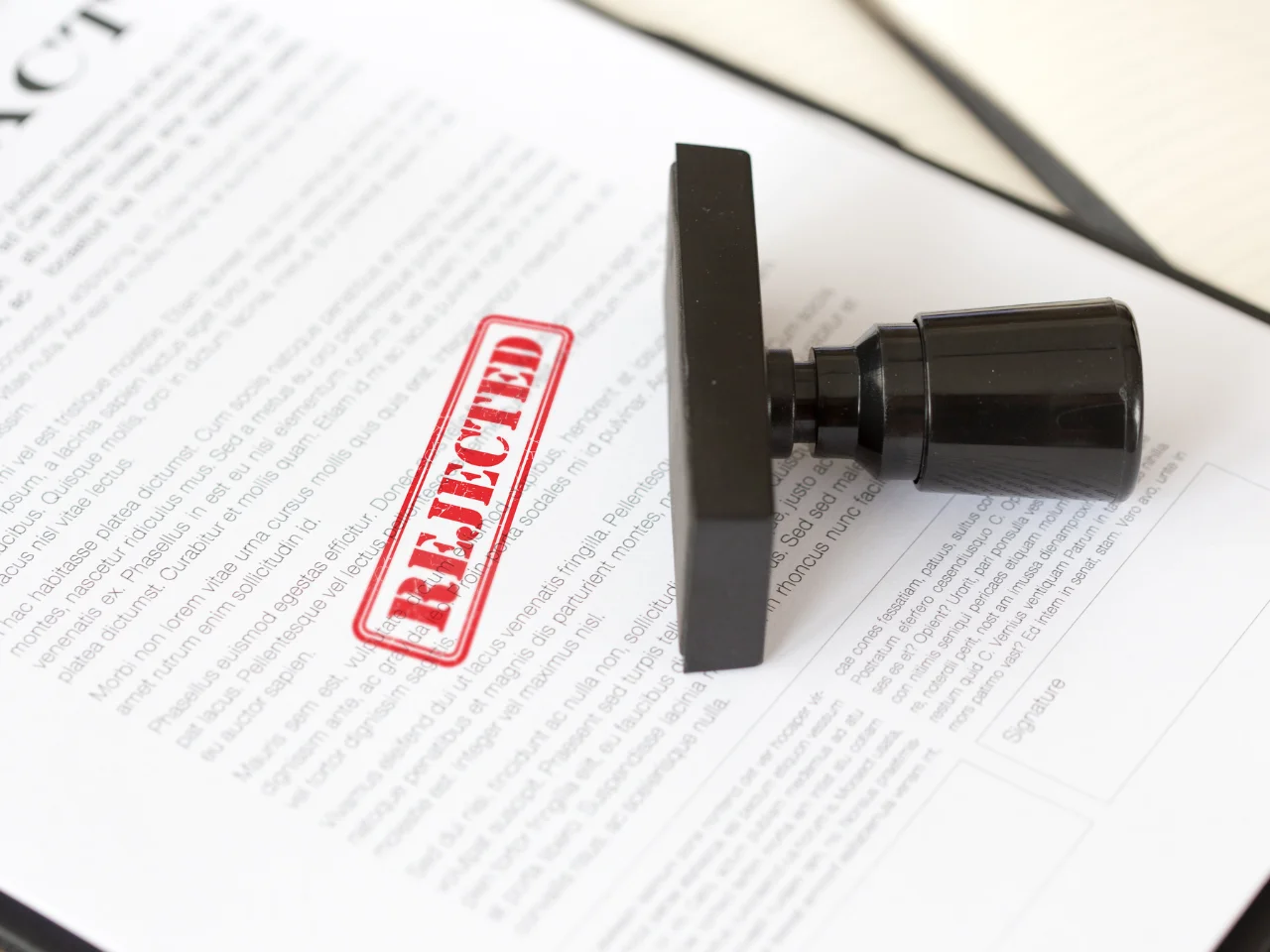 A contract document with a large red REJECTED stamp across it, and a black stamp lying on top of the paper.